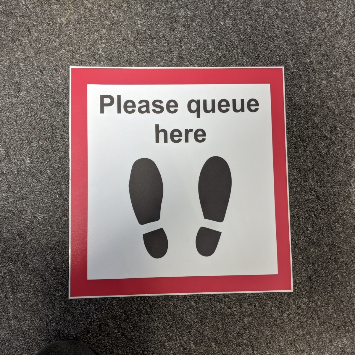 a square floor sticker informing customers where to stand when waiting