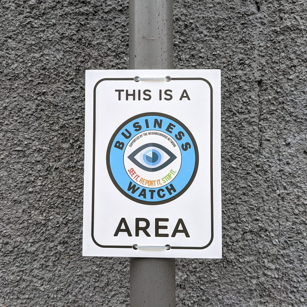 white & blue business watch sign mounted to a lamppost